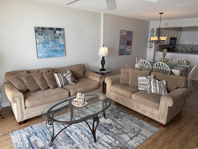 living area featuring a textured ceiling, wood finished floors, and ceiling fan with notable chandelier