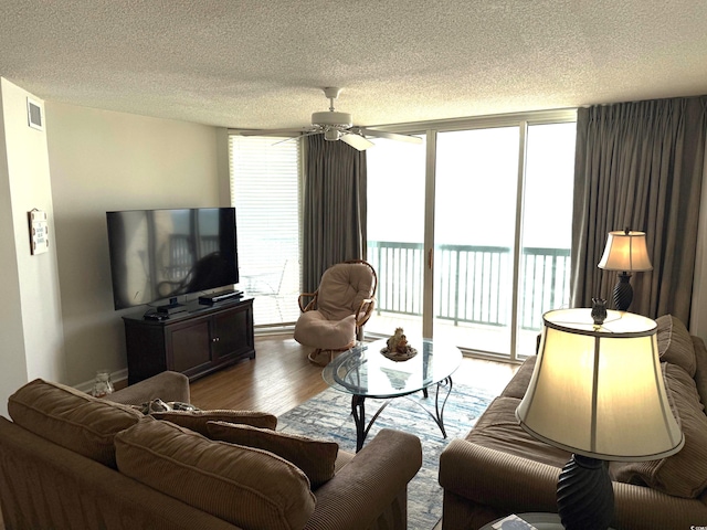 living area with a ceiling fan, plenty of natural light, wood finished floors, and a textured ceiling