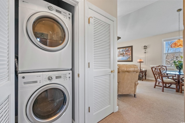 laundry area featuring stacked washer / dryer, light carpet, and baseboards