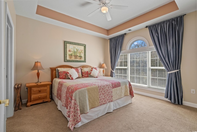 carpeted bedroom featuring baseboards, a raised ceiling, and a ceiling fan