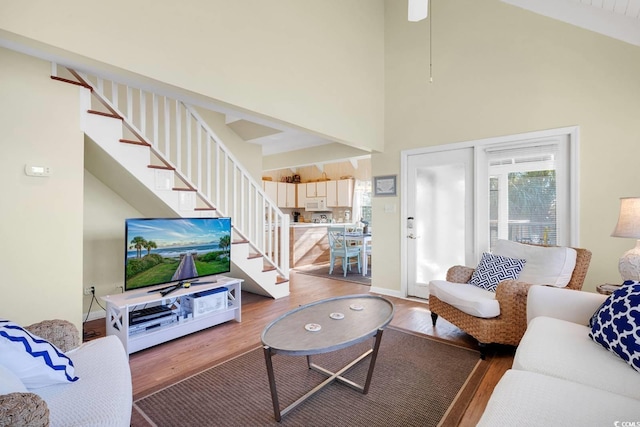 living area featuring light wood-style floors, a towering ceiling, baseboards, and stairway