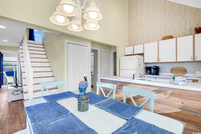 dining area with a high ceiling, a notable chandelier, recessed lighting, wood finished floors, and stairs