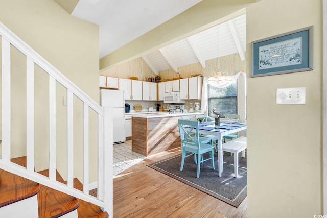 kitchen featuring lofted ceiling with beams, white appliances, a peninsula, light countertops, and light wood finished floors