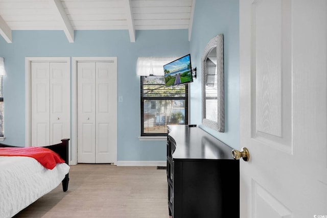 bedroom featuring light wood-style flooring, vaulted ceiling with beams, two closets, and baseboards