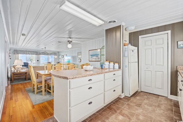kitchen with freestanding refrigerator, visible vents, ceiling fan, a peninsula, and white cabinets