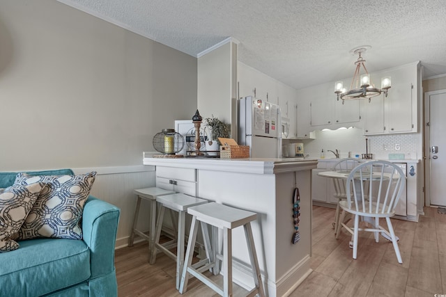 kitchen featuring a notable chandelier, light wood-style flooring, freestanding refrigerator, a wainscoted wall, and white cabinets