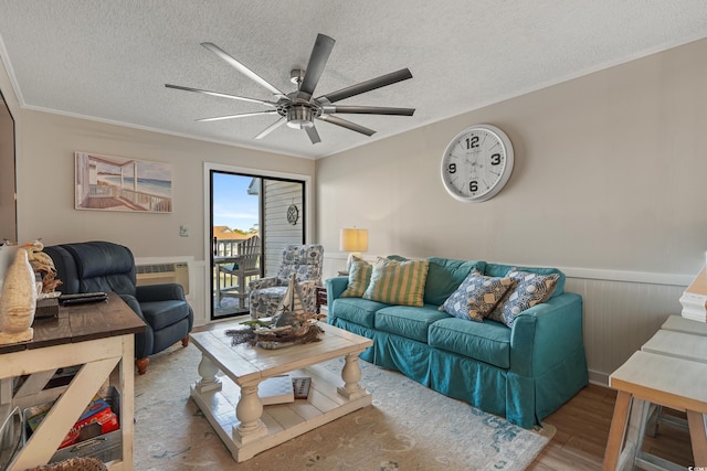 living area featuring ceiling fan, a textured ceiling, crown molding, wainscoting, and wood finished floors