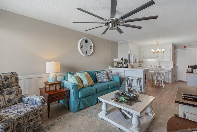 living area with a textured ceiling, wainscoting, light wood-style floors, and ceiling fan with notable chandelier