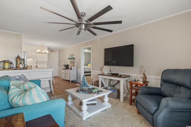 living area featuring crown molding, ceiling fan with notable chandelier, light wood-style floors, a textured ceiling, and a wainscoted wall