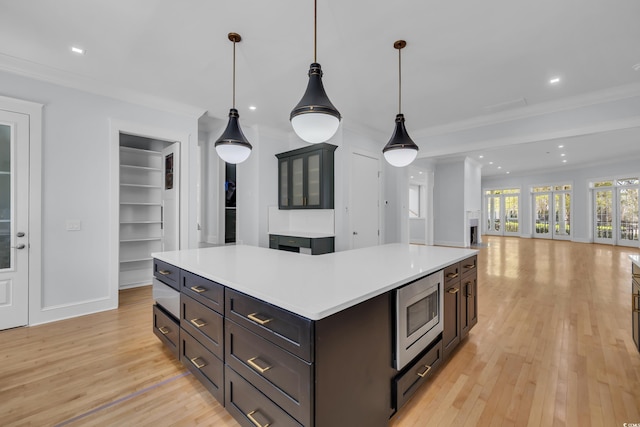 kitchen featuring stainless steel microwave, light wood-style flooring, light countertops, and ornamental molding