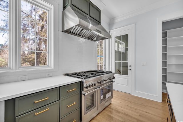 kitchen featuring light wood-type flooring, crown molding, extractor fan, green cabinetry, and range with two ovens