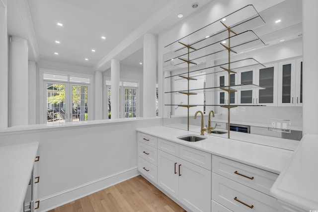 kitchen with glass insert cabinets, light wood-type flooring, white cabinets, light countertops, and a sink