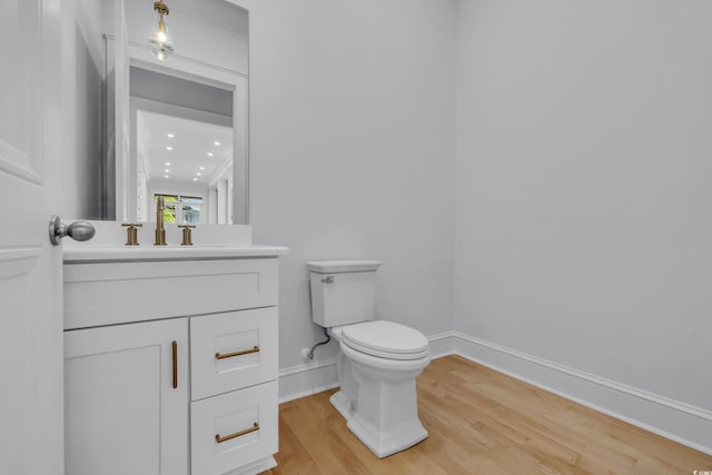 half bath featuring toilet, wood finished floors, vanity, and baseboards