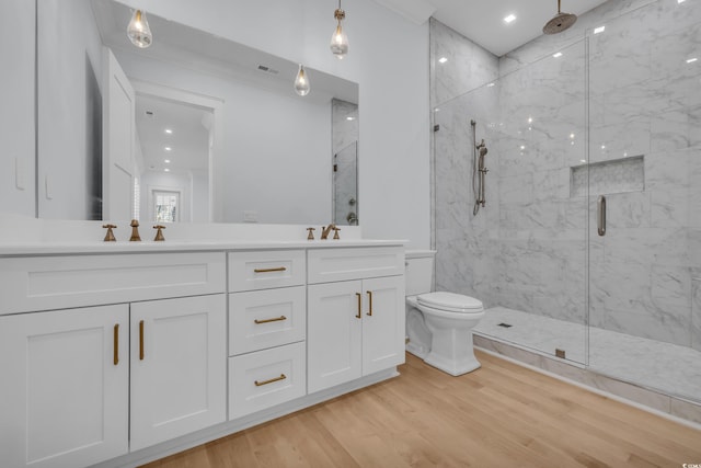 bathroom featuring toilet, wood finished floors, a sink, a marble finish shower, and double vanity