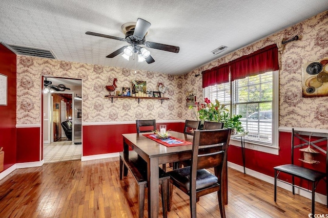 dining area with a textured ceiling, wallpapered walls, wainscoting, and visible vents