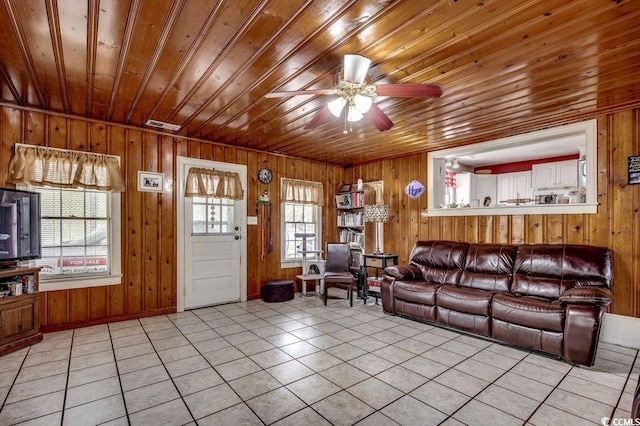 living area featuring wood walls, wooden ceiling, light tile patterned floors, and a ceiling fan