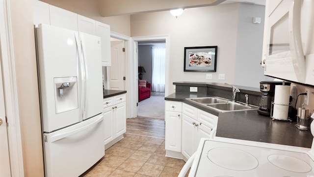 kitchen with white fridge with ice dispenser, a sink, dark countertops, white cabinetry, and stove