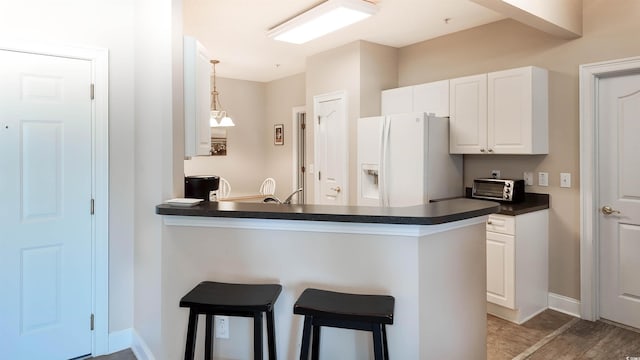 kitchen with a peninsula, white refrigerator with ice dispenser, dark countertops, white cabinets, and a breakfast bar area