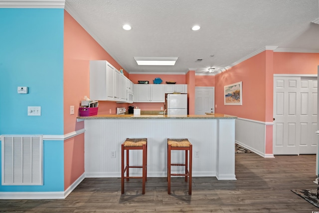kitchen with visible vents, freestanding refrigerator, a peninsula, white cabinetry, and dark wood-type flooring