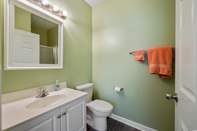 bathroom featuring a shower with shower door, vanity, toilet, wood finished floors, and baseboards