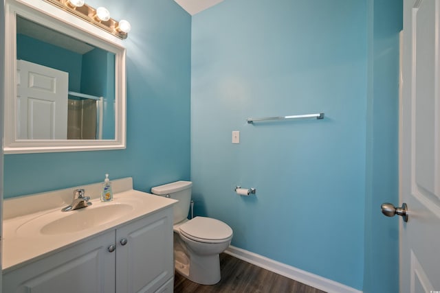 bathroom with baseboards, toilet, vanity, wood finished floors, and a shower with shower door