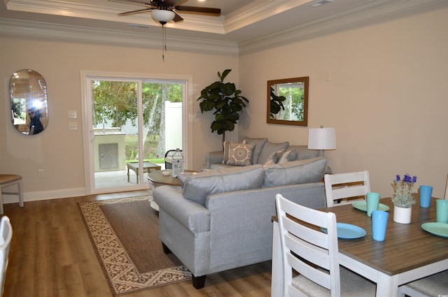 living room featuring ceiling fan, a raised ceiling, wood finished floors, ornamental molding, and baseboards