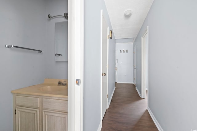 hall featuring a sink, baseboards, and dark wood-style floors