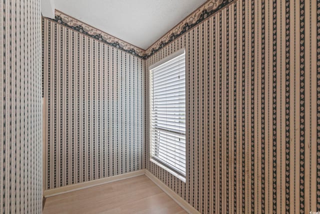 interior space featuring baseboards, light wood-type flooring, wallpapered walls, and a textured ceiling