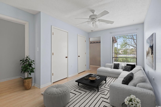 living room featuring a textured ceiling, wood finished floors, ceiling fan, and baseboards