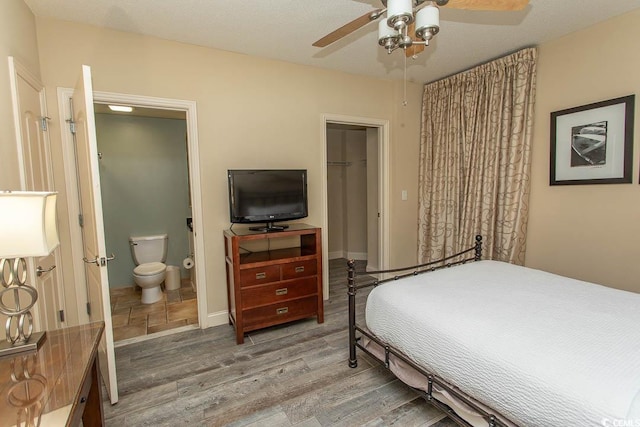 bedroom featuring a walk in closet, a ceiling fan, wood finished floors, a closet, and connected bathroom