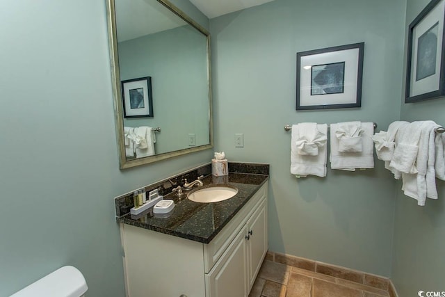 bathroom featuring baseboards, toilet, stone tile flooring, and vanity