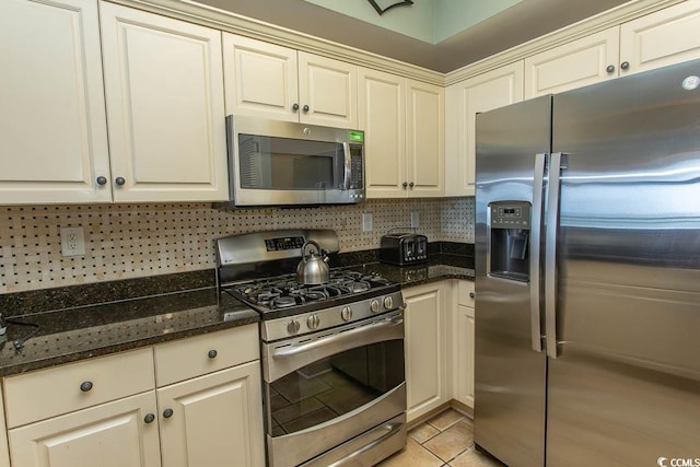 kitchen with light tile patterned floors, appliances with stainless steel finishes, backsplash, and dark stone countertops