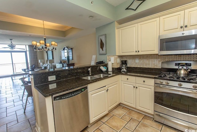 kitchen with a sink, stainless steel appliances, a peninsula, a tray ceiling, and stone tile flooring