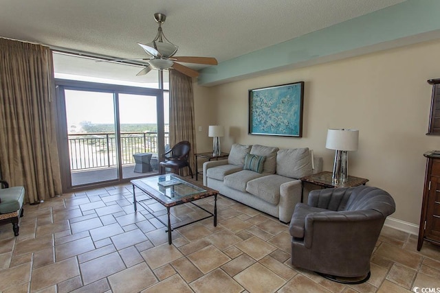 living area with a textured ceiling, ceiling fan, baseboards, and stone tile flooring