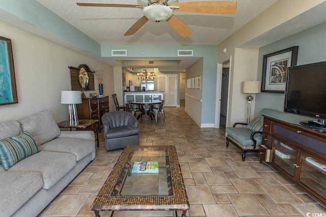 living area featuring visible vents, baseboards, ceiling fan with notable chandelier, and stone tile flooring