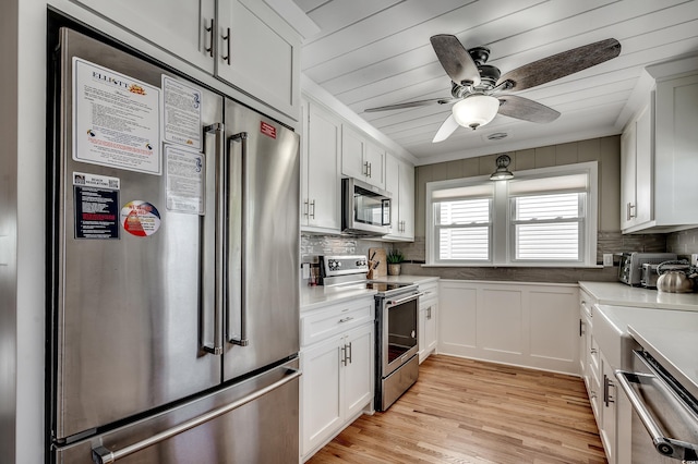 kitchen with light wood-style flooring, white cabinetry, a ceiling fan, stainless steel appliances, and decorative backsplash