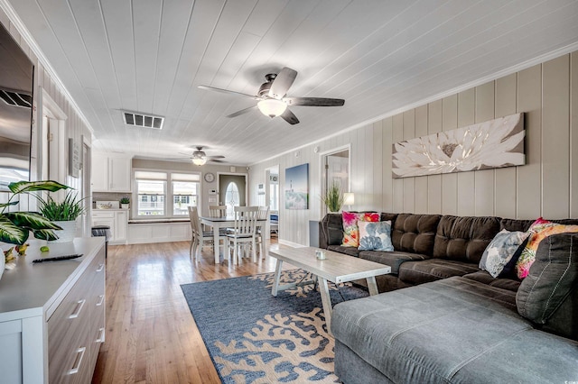 living area featuring light wood-style floors, visible vents, a ceiling fan, and ornamental molding