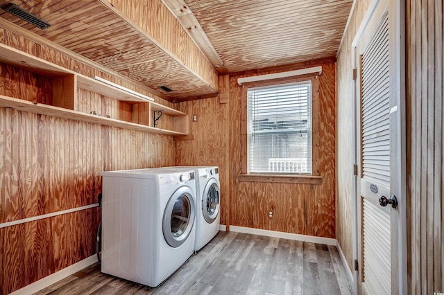 laundry room featuring laundry area, wood ceiling, wood finished floors, wood walls, and washing machine and clothes dryer