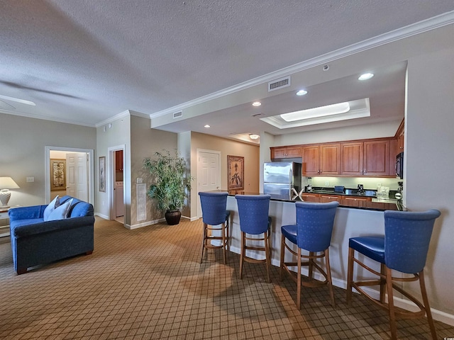 kitchen with visible vents, dark countertops, freestanding refrigerator, a tray ceiling, and a breakfast bar area