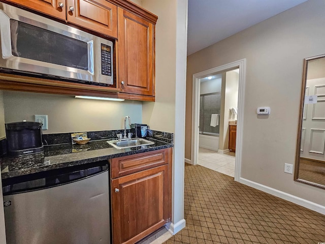 kitchen featuring brown cabinetry, dark stone countertops, appliances with stainless steel finishes, a sink, and baseboards