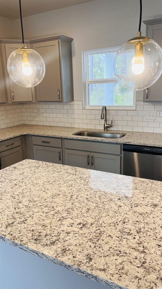kitchen with a sink, gray cabinetry, light stone countertops, stainless steel dishwasher, and decorative backsplash