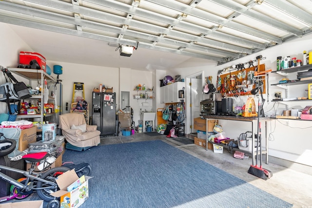 garage featuring black fridge with ice dispenser, a garage door opener, electric panel, and a workshop area