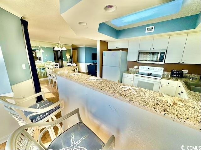 kitchen with a sink, visible vents, white cabinetry, white appliances, and light stone counters