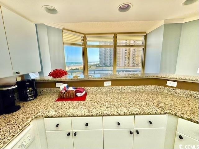 kitchen with light stone countertops, crown molding, and white cabinetry