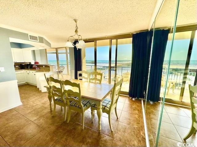 tiled dining room featuring a textured ceiling, a water view, visible vents, a chandelier, and expansive windows