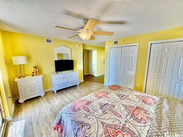 bedroom featuring wood finished floors, multiple closets, visible vents, and a textured ceiling