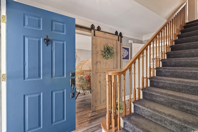entryway featuring wood finished floors, ornamental molding, a barn door, and stairway