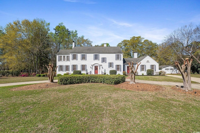 colonial house featuring a chimney, a front lawn, and concrete driveway