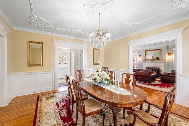dining room featuring wood finished floors, a warm lit fireplace, a notable chandelier, and crown molding