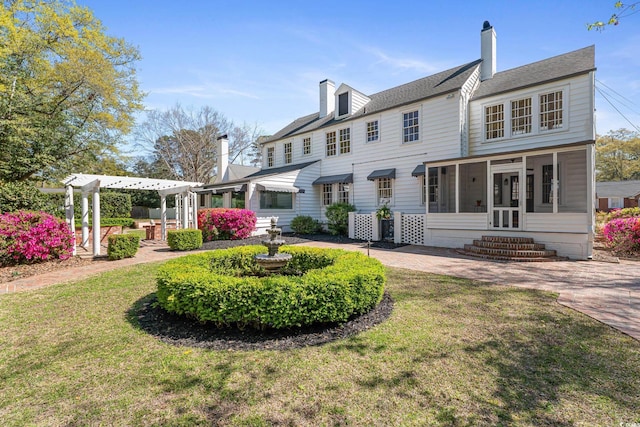 rear view of house featuring a lawn, a sunroom, a chimney, and a pergola
